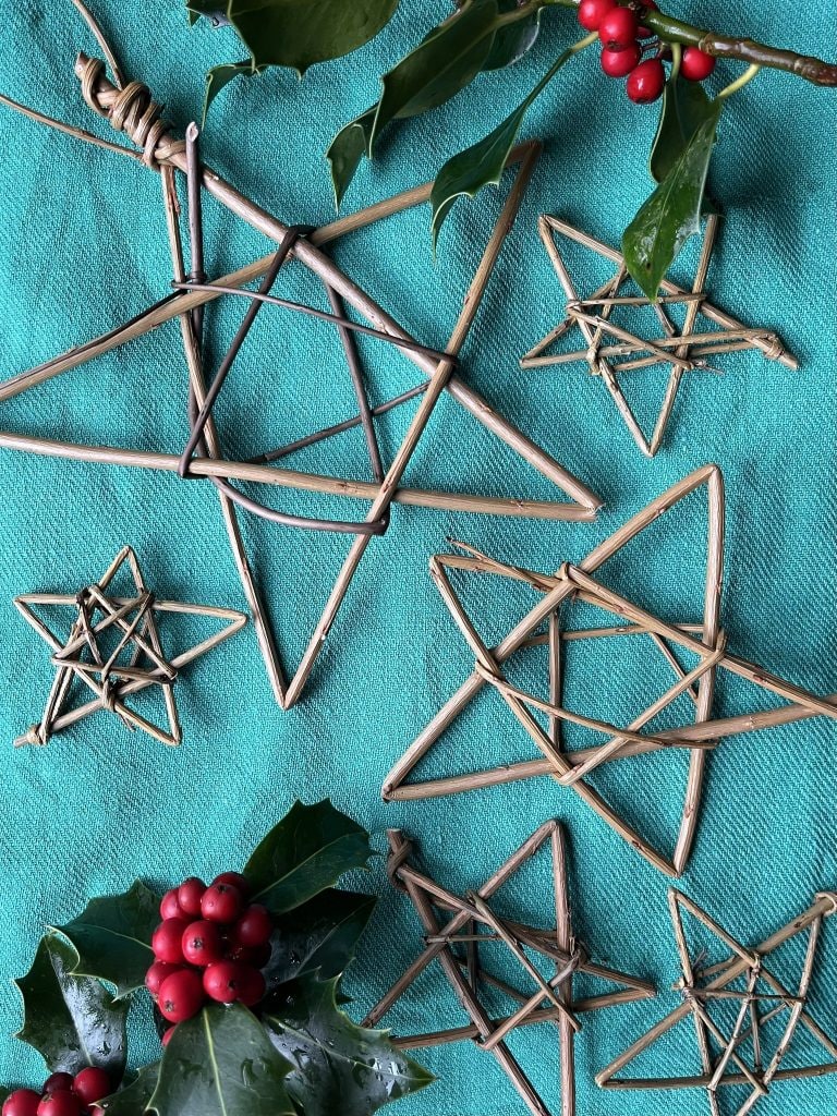 Handmade straw stars with holly and red berries on turquoise fabric, perfect for festive decorations.
