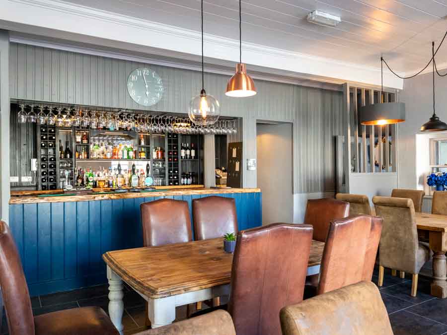 Cozy bar and dining area with a variety of seating, bar stools, and a well-stocked bar in a modern, stylish pub.