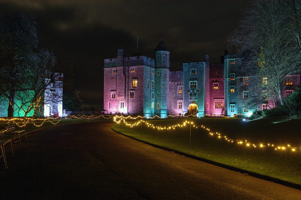 An illuminated historic castle at night with colourful lighting and festive fairy lights.