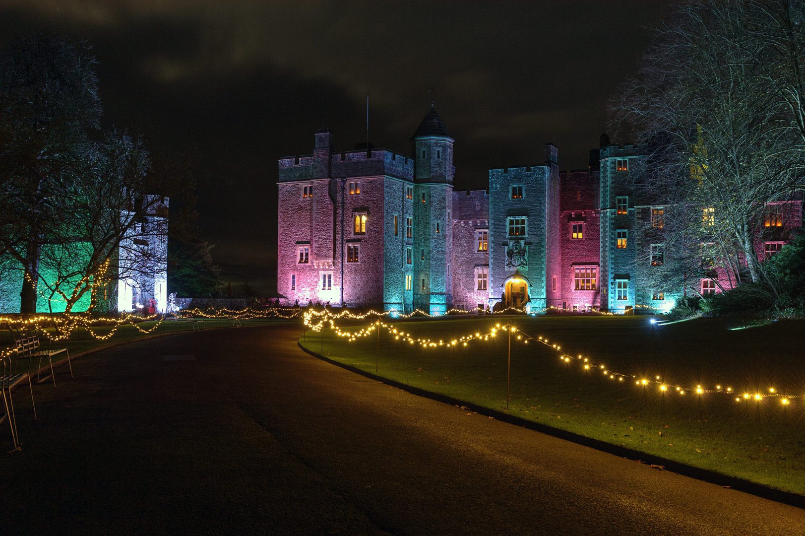 An illuminated historic castle at night with colourful lighting and festive fairy lights.