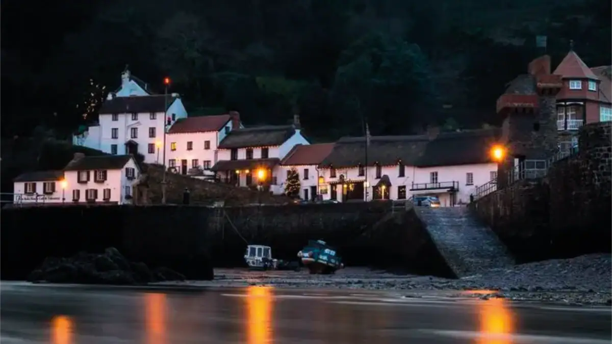 Night-time view of Lynmouth harbour and coastline beside The Rising Sun, illuminated with warm reflections on the water