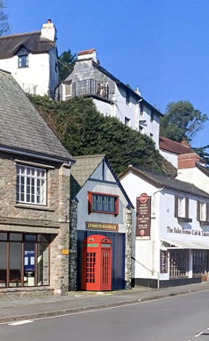 A colourful traditional red phone box sits between local shops in Lynmouth, Exmoor National Park.