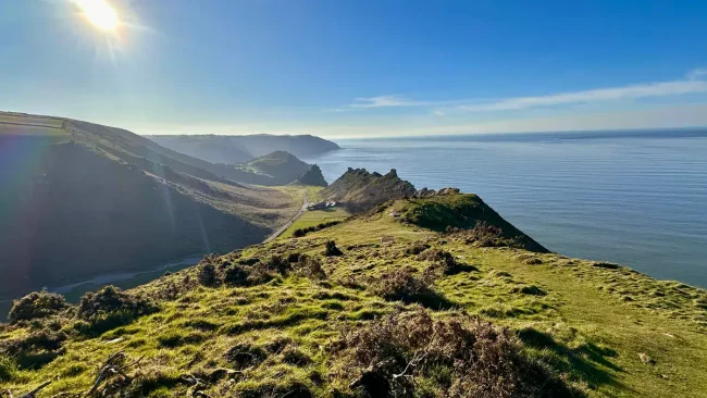 Wake Up to Spring in Stunning Exmoor coastline with lush green hills and blue ocean under clear skies.
