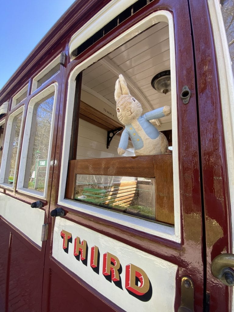 Vintage train carriage with a stuffed rabbit toy looking out the window.