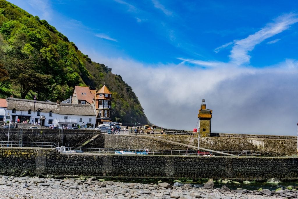 Lynmouth harbour with colourful buildings and cliffs under a blue sky.