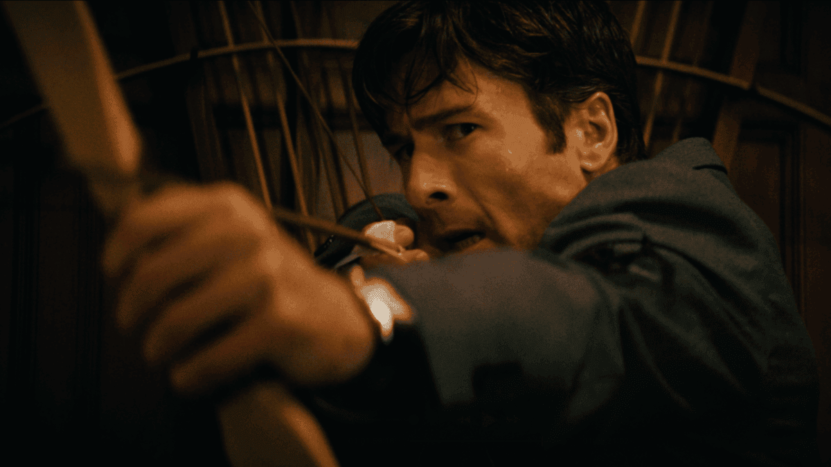 A tense moment featuring a man hiding in a dark, wooden setting, looking cautiously over his shoulde.