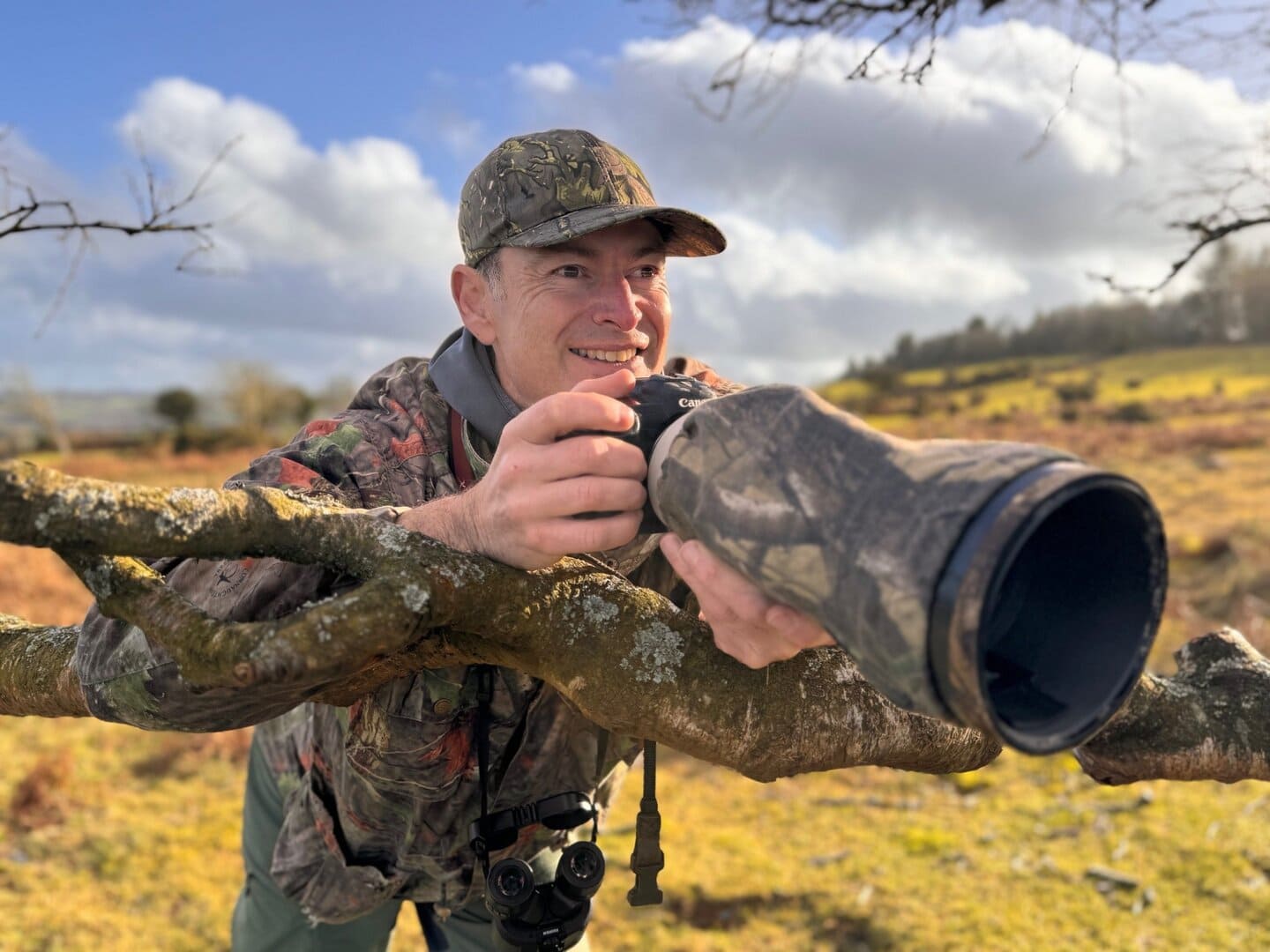 Photographer with camera in nature, capturing wildlife in a rural landscape.