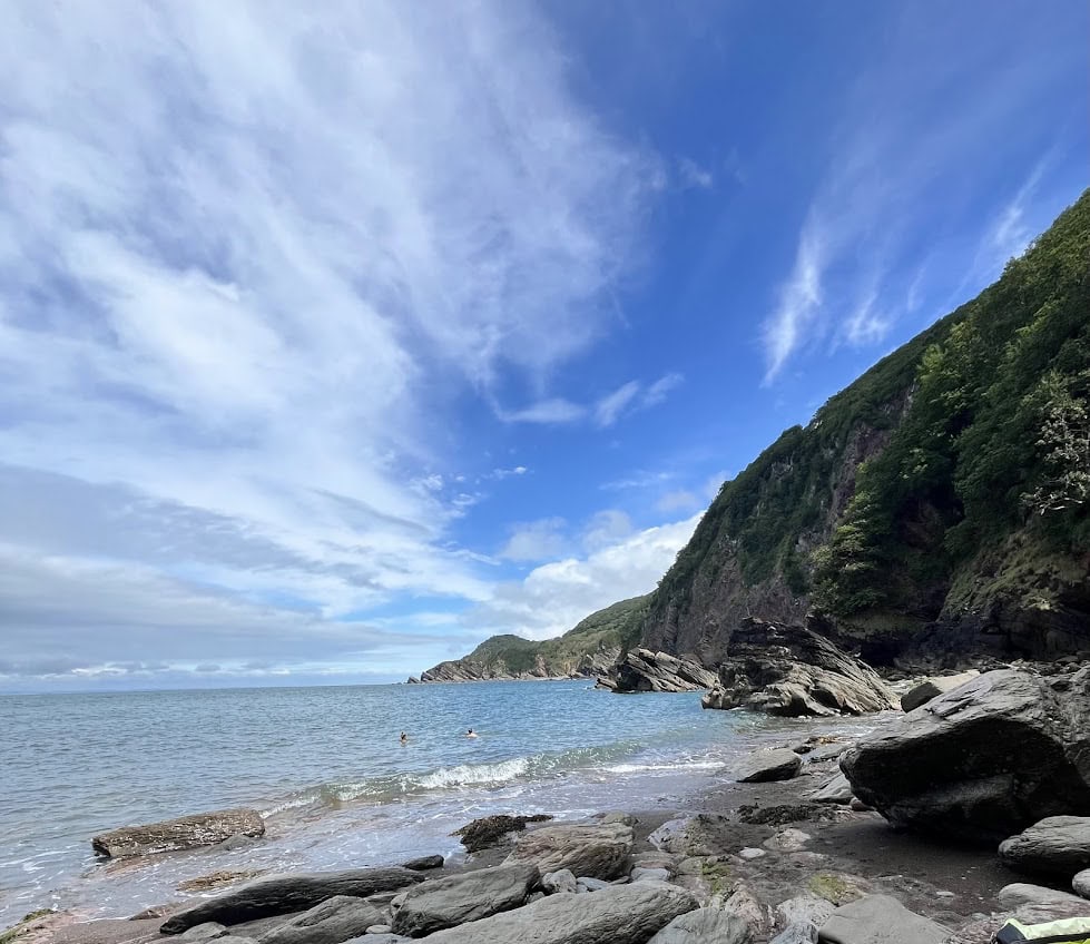 Seaside rocky shoreline with cliffs and blue sky, part of Exmoor National Park.