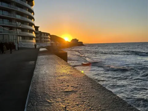 Sunset paints the skies over Little Switzerland, with waves crashing and modern hotels alongside scenic views.